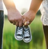 woman and man holding black crib shoes standing near green grass during daytime