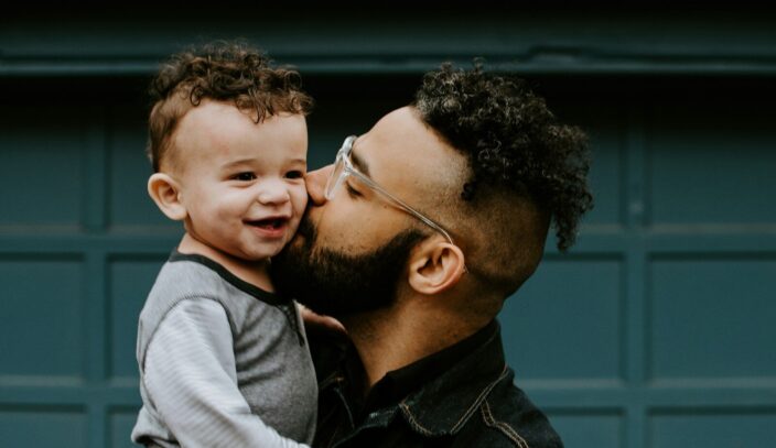 man carrying baby boy and kissing on cheek